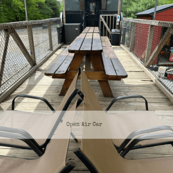 Wooden table on a bridge with benches, train car in background.