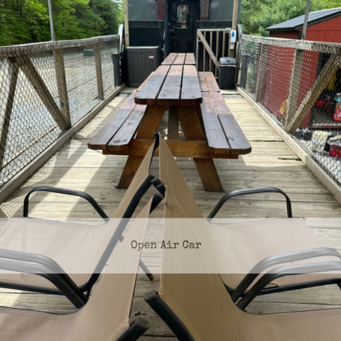 Wooden table on a bridge with benches, train car in background.