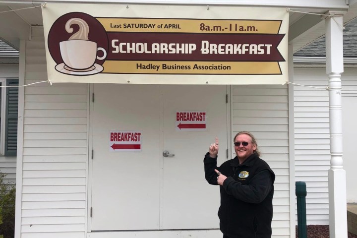 Person pointing at a 'Scholarship Breakfast' banner on a building.