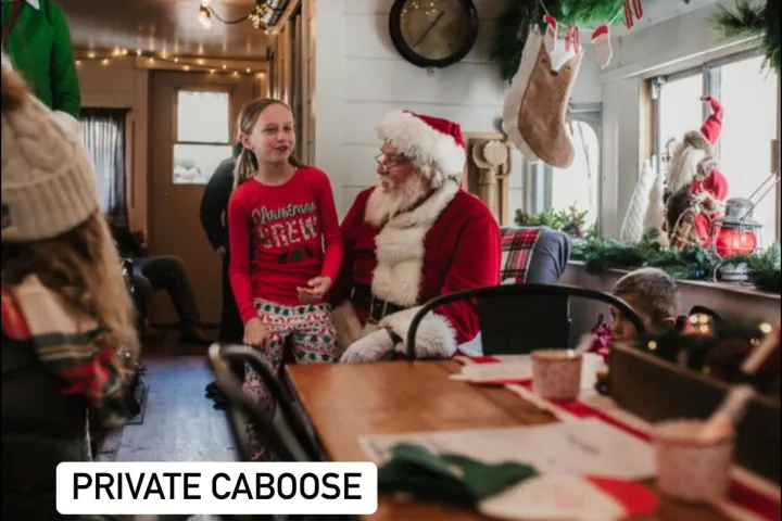 Child in Santa outfit talking to Santa claus on a decorative train caboose.