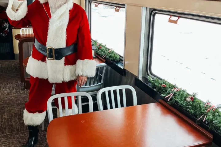 Santa waving in a festively decorated train car with garlands and candy canes.