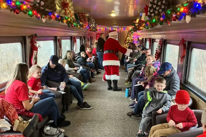 Train car interior with Santa, festive lights, passengers seated on either side.