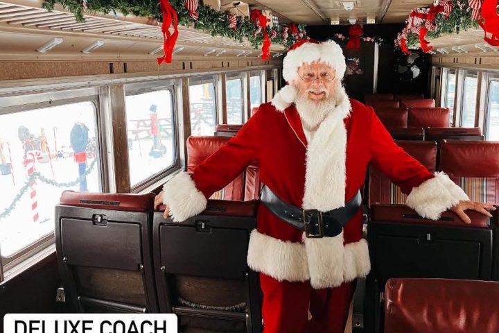 Santa in a decorated train car with red ribbons and greenery.