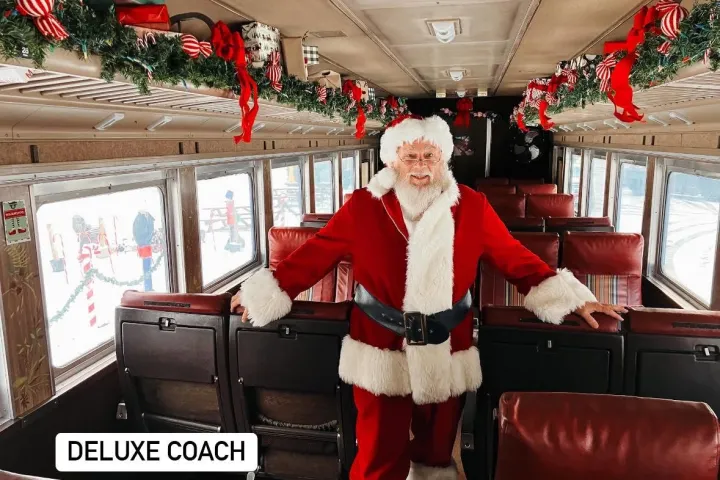 Santa in a decorated train car with red ribbons and greenery.