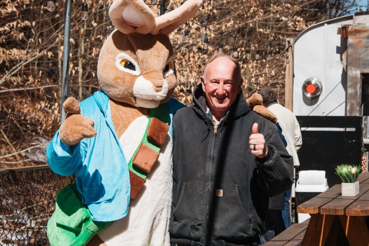 Man posing with a person in a bunny costume near picnic tables outdoors.