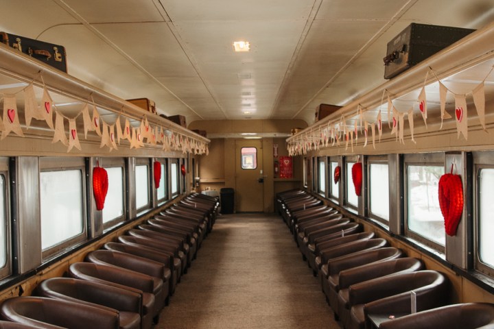 Empty vintage train car with brown seats and heart decorations hanging from the ceiling.