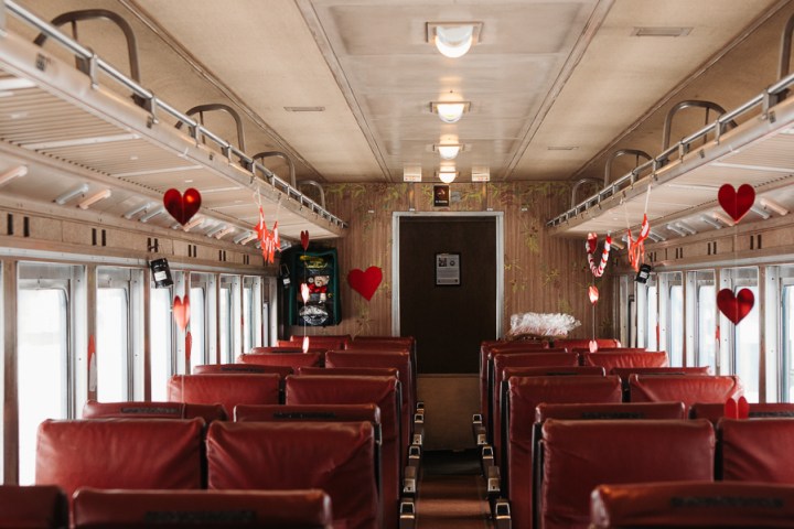 Empty train carriage with red seats and hanging heart decorations along the aisle.