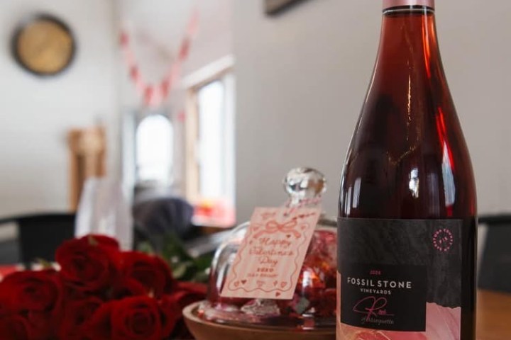 Red wine bottle and roses on a checkered tablecloth, with Valentine's Day decor.