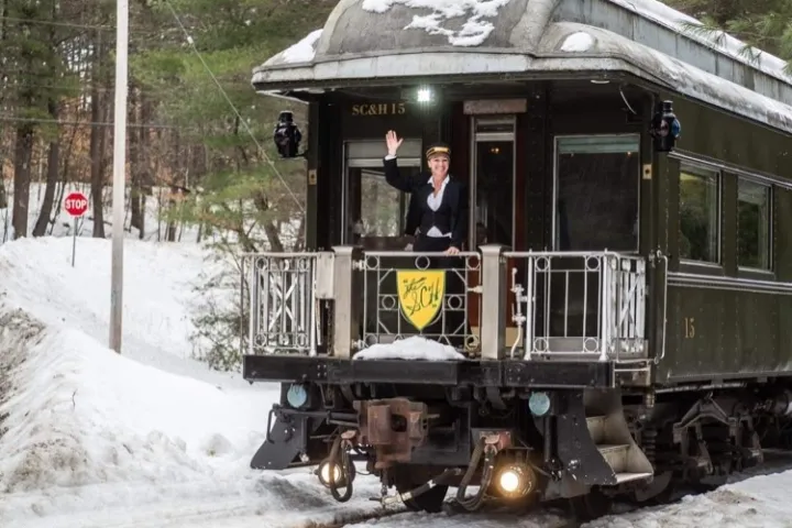 Person waving from the back of a vintage train car in snowy landscape.