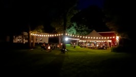 Night scene with string lights over a tent and people gathered around a campfire.