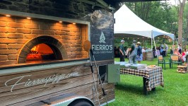 Pizza oven trailer at outdoor event with people under a white tent.