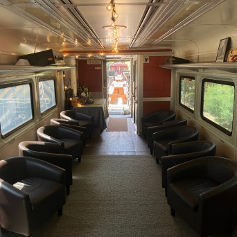 Interior of a train car with rows of black chairs and large windows.