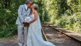 Bride and groom kissing on a railroad track surrounded by trees.
