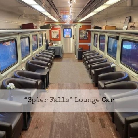 Interior of a train lounge car with rows of gray chairs and wood flooring.